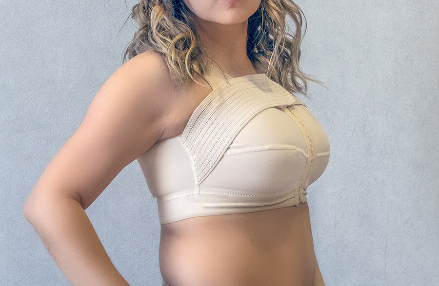 Young woman in beige compression bra bandage after breast augmentation surgery.