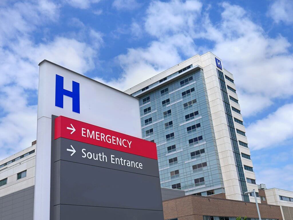 A Hospital sign as seen from the parking lot, with the hospital in the background.