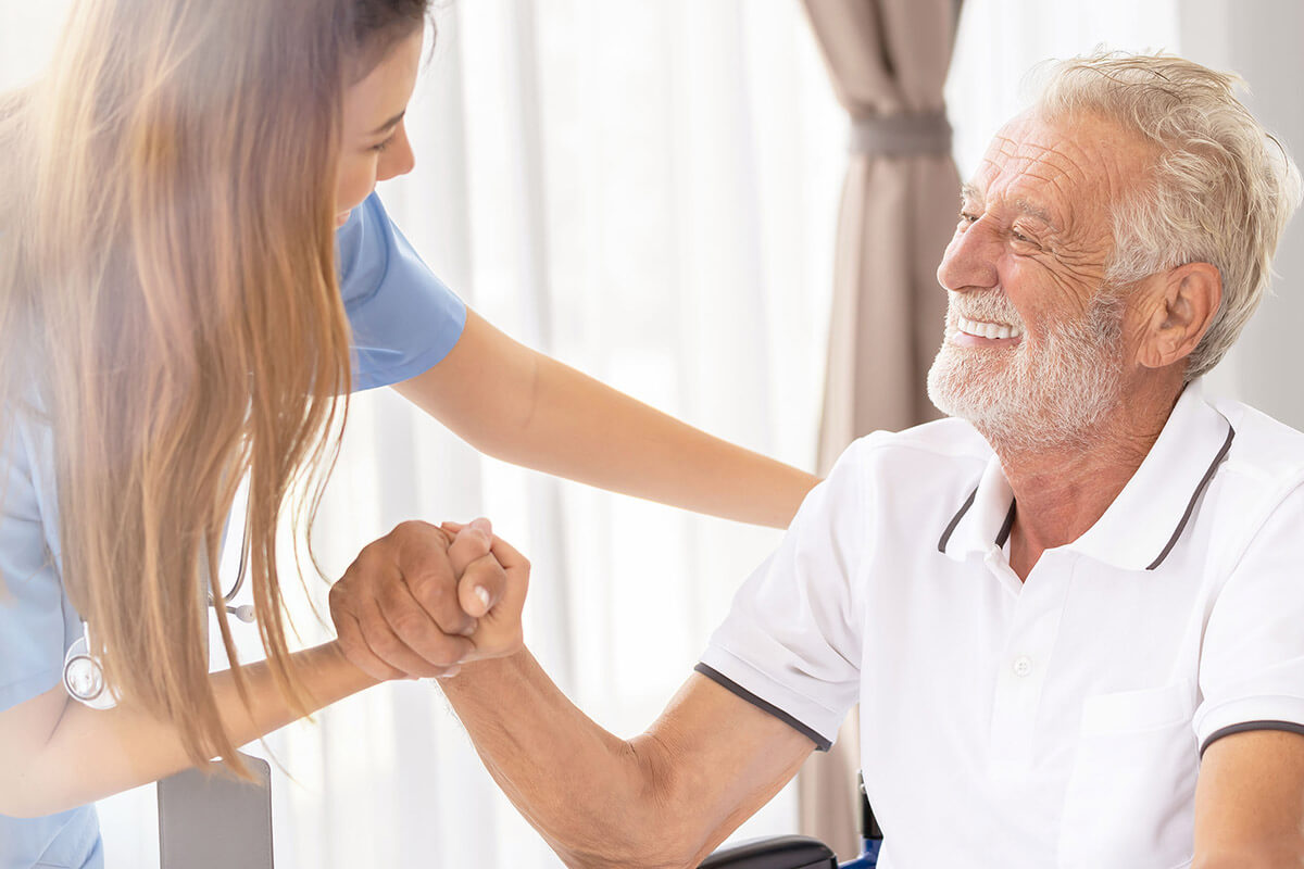 A nurse assisting a laughing elderly man.