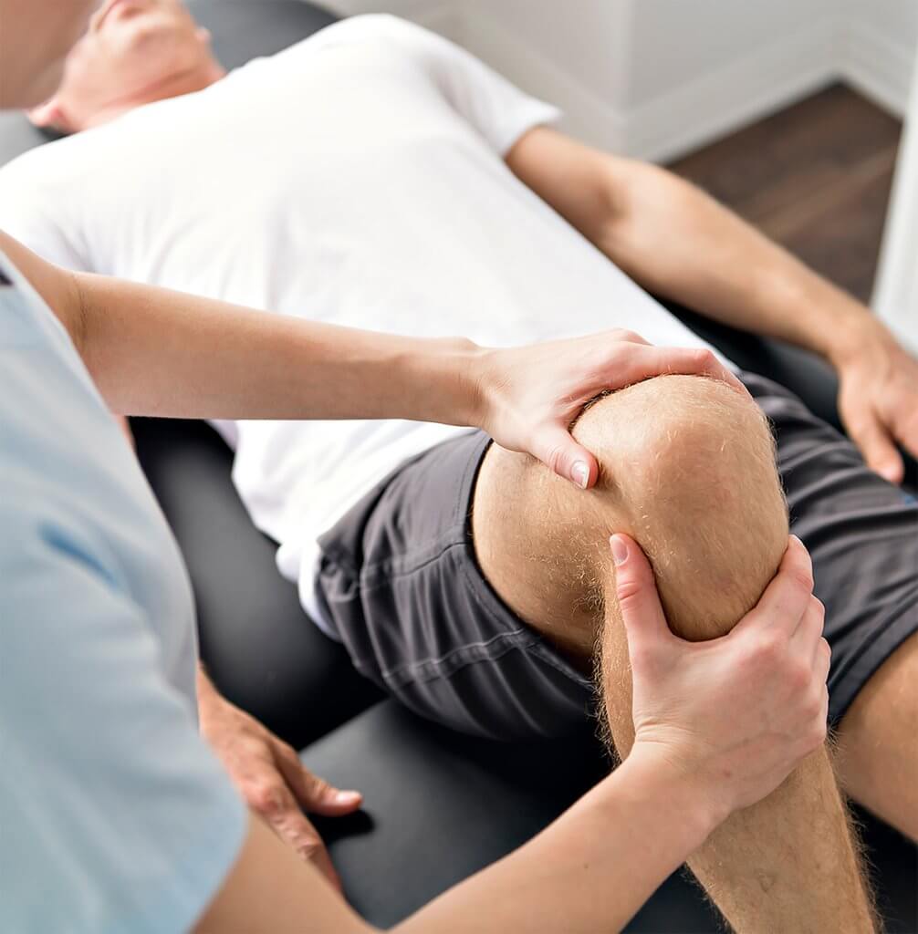 A physical therapist manually examines a patient's knee during a rehabilitation session at a Proliance Surgeons physical therapy clinic