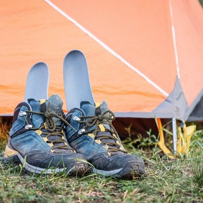 A pair of wet and dirty hiking boots are drying near the tent with the insole sticking out