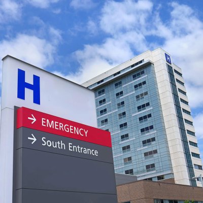 A Hospital sign as seen from the parking lot, with the hospital in the background.