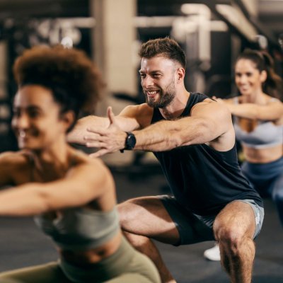 Fit friends in a squat position exercising with an instructor in a gym.