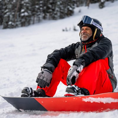 Portrait of an African-American man in his fifties sitting on the snow with his snowboard strapped to his feet at a ski resort in Winter Park, Colorado.